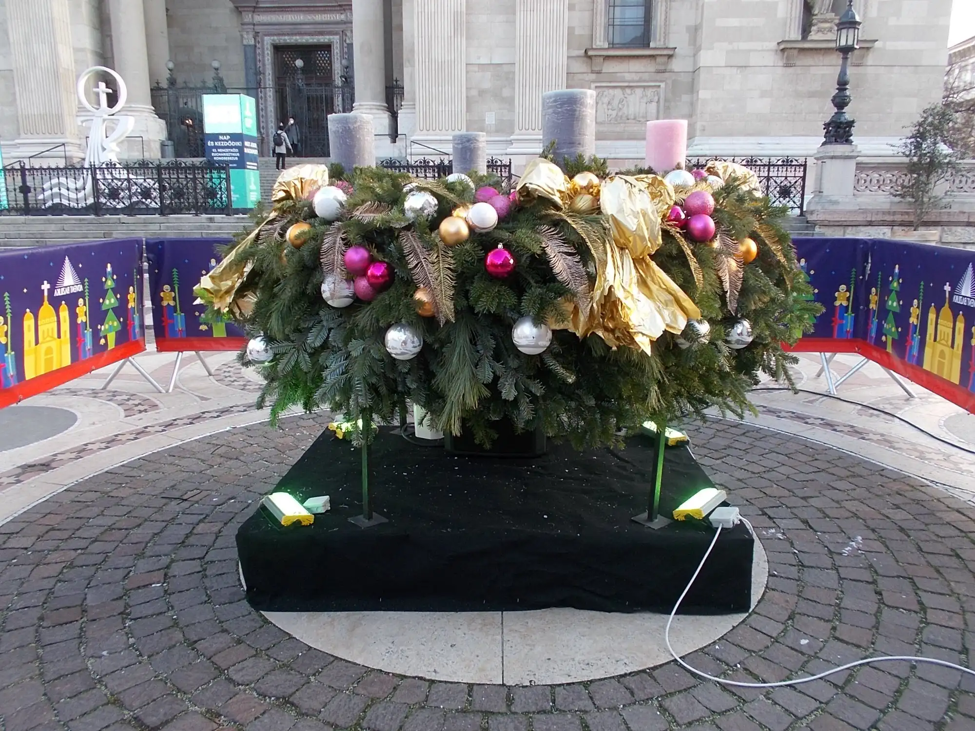 The large Advent wreath of greenery, gold ribbon and baubles with four tall candles, on a platform in front of the steps of St Stephen's Basilica