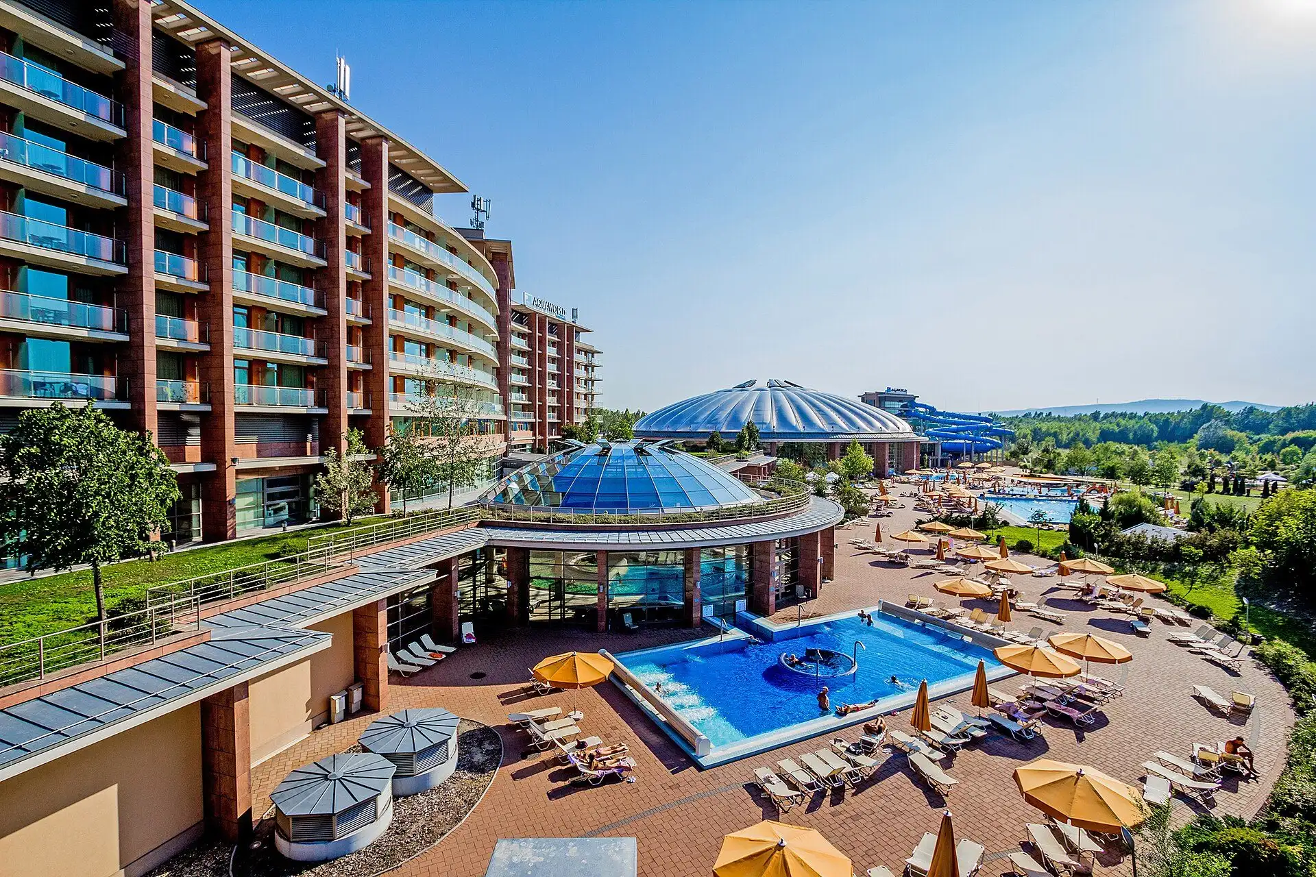 The outdoor summer pools at Aquaworld, with sunshades and loungers beside the hotel and the dome behind