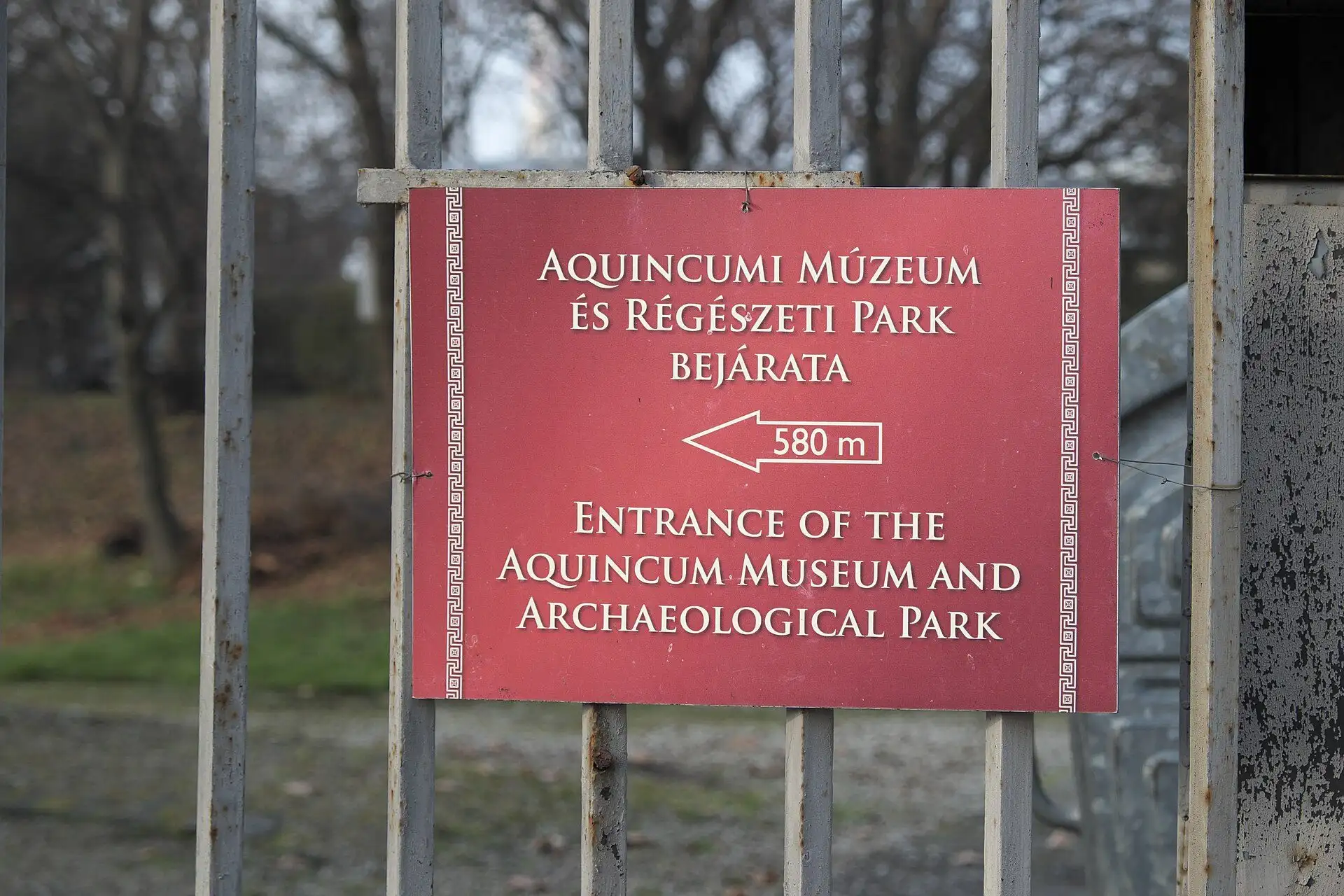 The red sign on the street fence pointing to the entrance of the Aquincum Museum and Archaeological Park, 580 m away