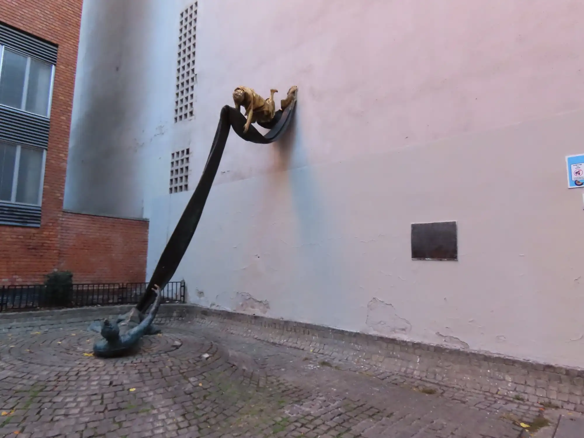 The Carl Lutz memorial on Dob utca in Budapest, a gilded figure on a wall lowering a long bronze cloth to a figure lying on the cobbles below