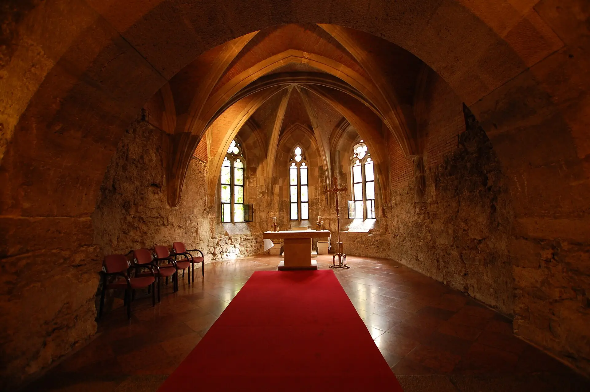 The vaulted medieval chapel crypt under the royal palace at the Budapest History Museum, with lancet windows behind the altar and a red carpet down the middle