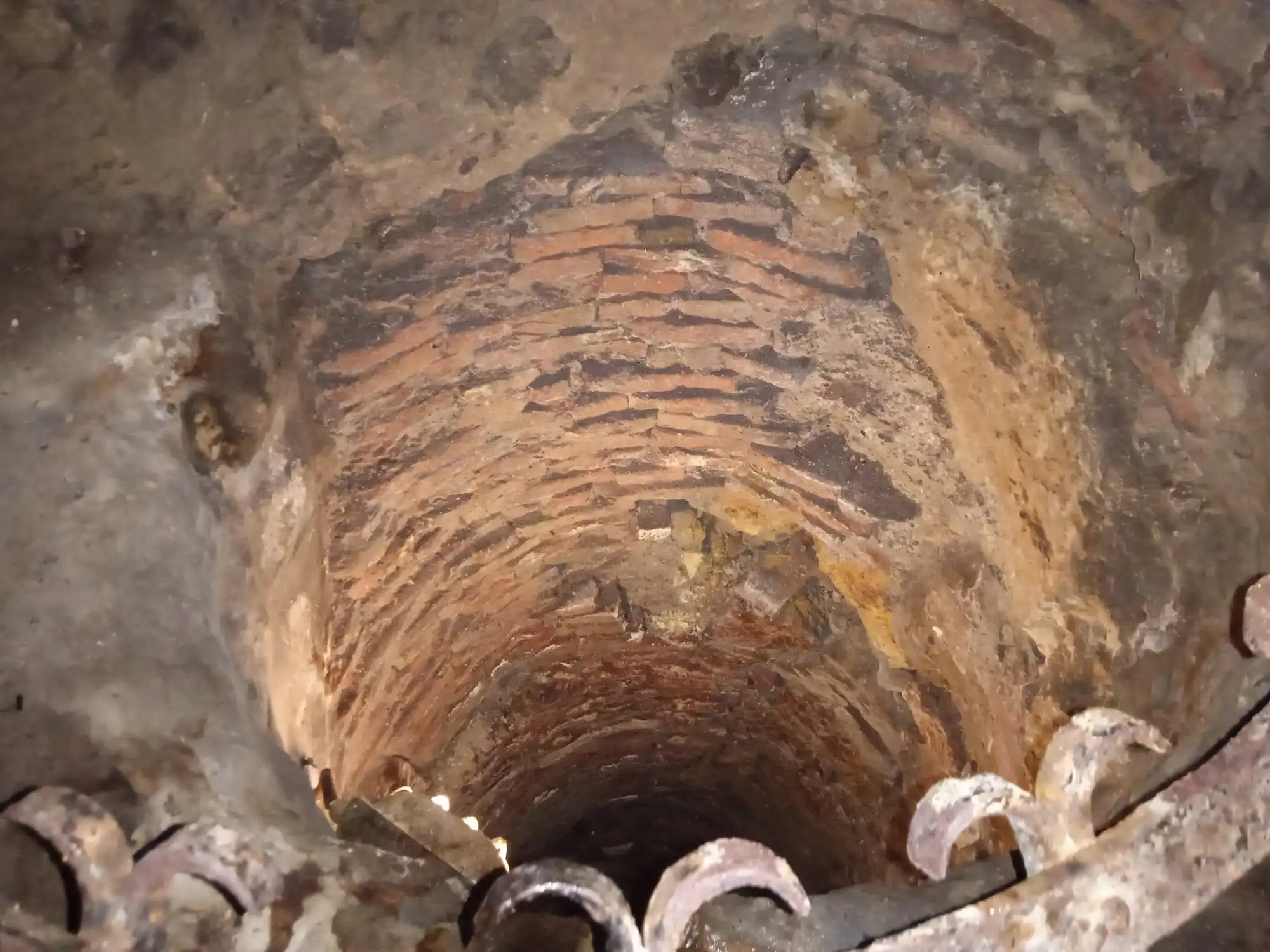 Looking down a brick-lined shaft through an iron grille in the Buda Castle Cave