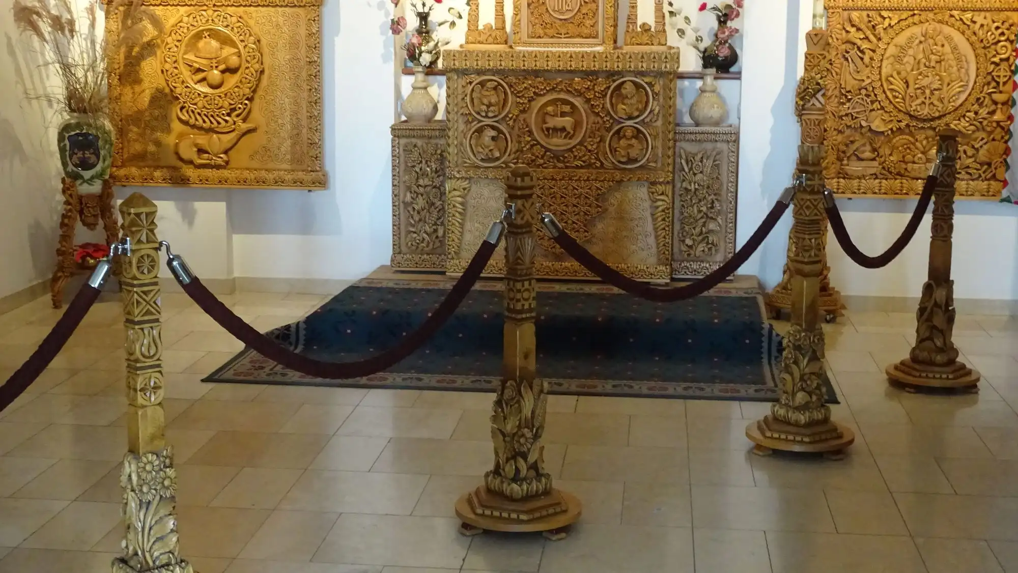 Intricately carved wooden panels and an ornate carved wooden altar, behind a low rope barrier on carved wooden posts, in a white-walled hall of the Cave Church
