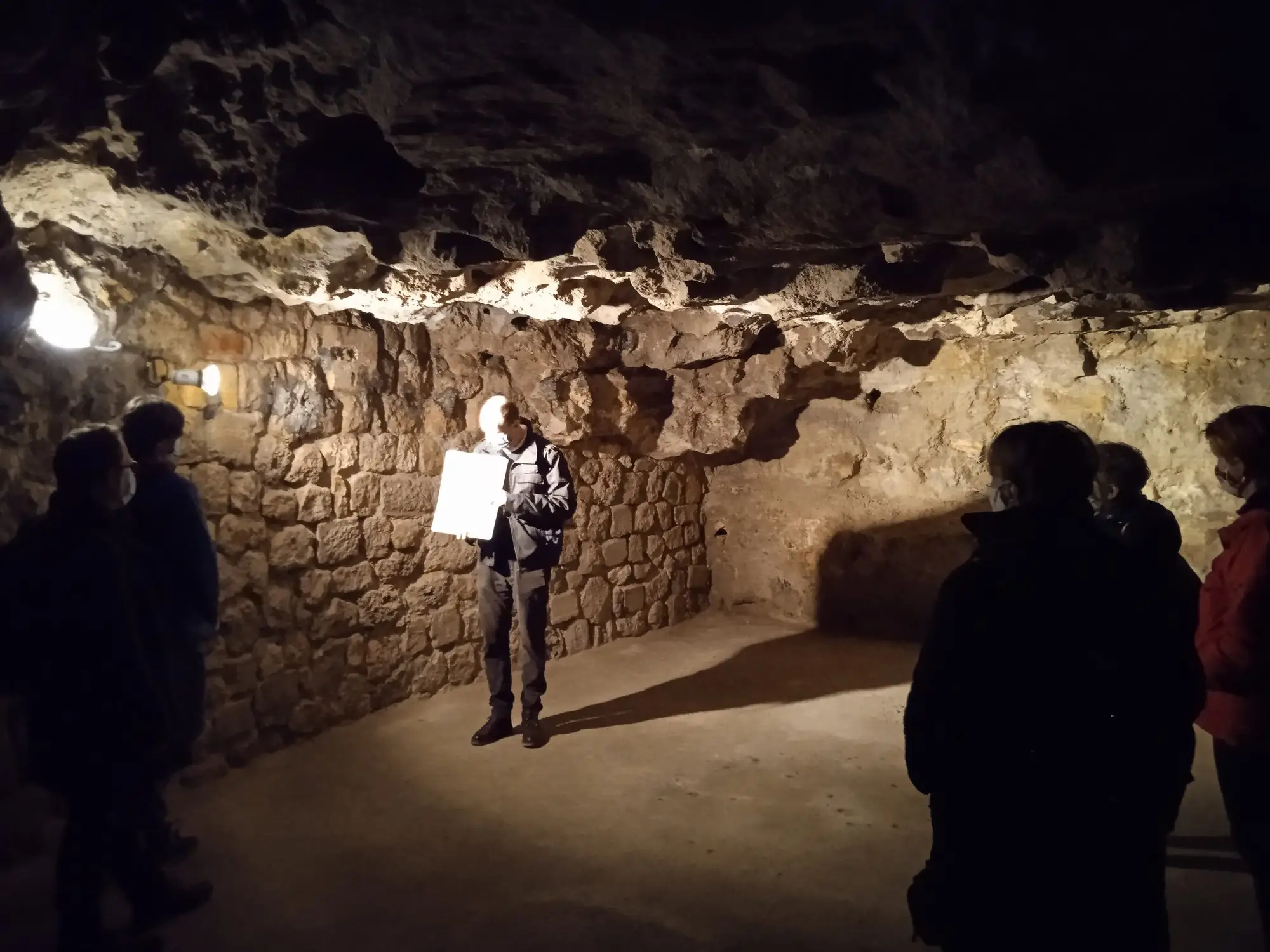 A guided group standing in a stone-walled corridor of the Buda Castle Cave under low lighting