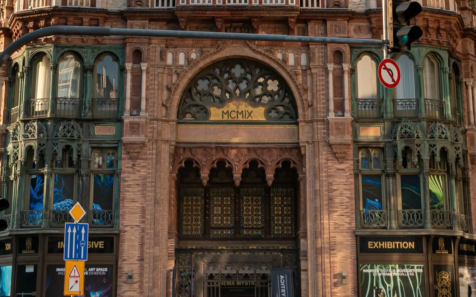 The arched corner doorway of the Párisi Udvar on Ferenciek tere, with a Cinema Mystica sign over the door and Immersive and Exhibition signs in the windows either side