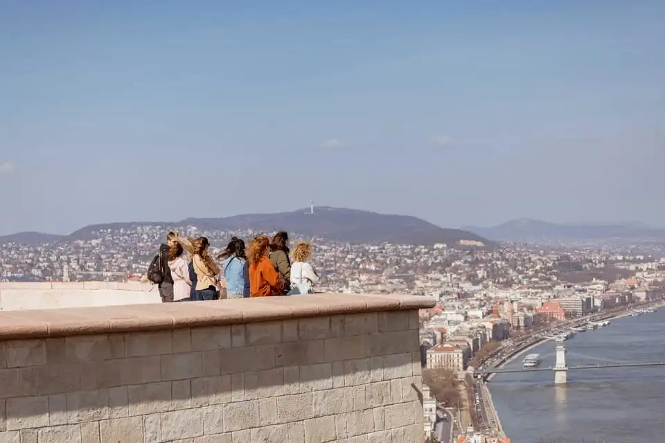 A group standing at a stone parapet on the Citadella's wall-walk, looking out over the Danube, the Chain Bridge and Pest