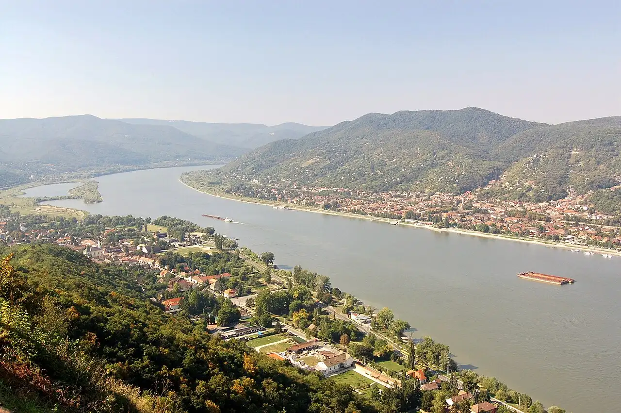 The Danube Bend seen from Visegrád Castle, the river running between wooded hills with small towns along both banks and a barge on the water