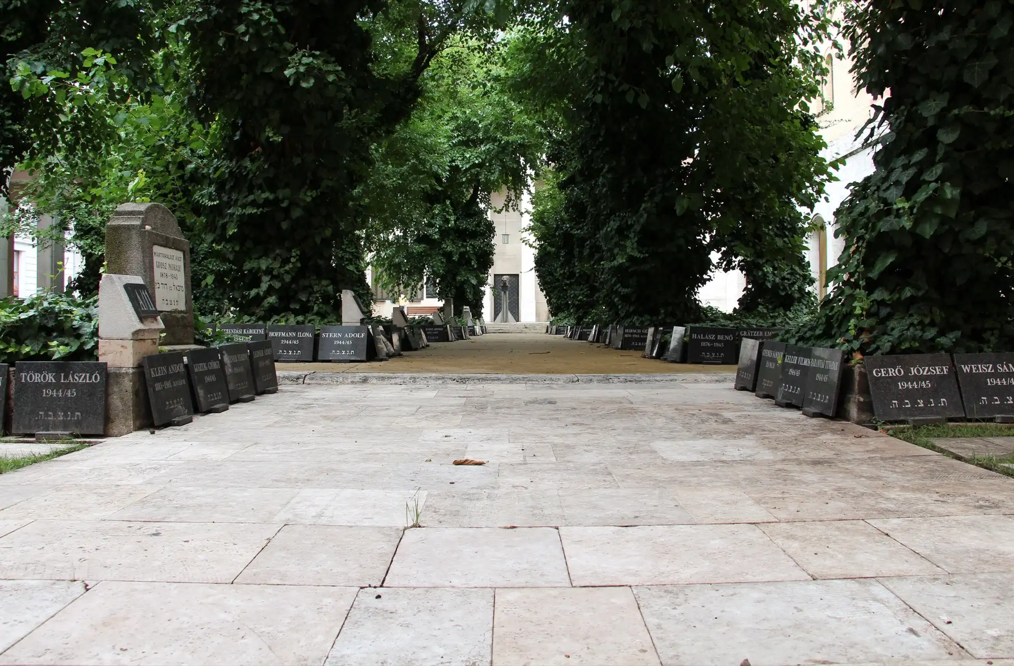 The cemetery garden beside the Dohány Street Synagogue, with rows of dark memorial stones under the trees and the entrance of the Heroes' Temple at the end of the path