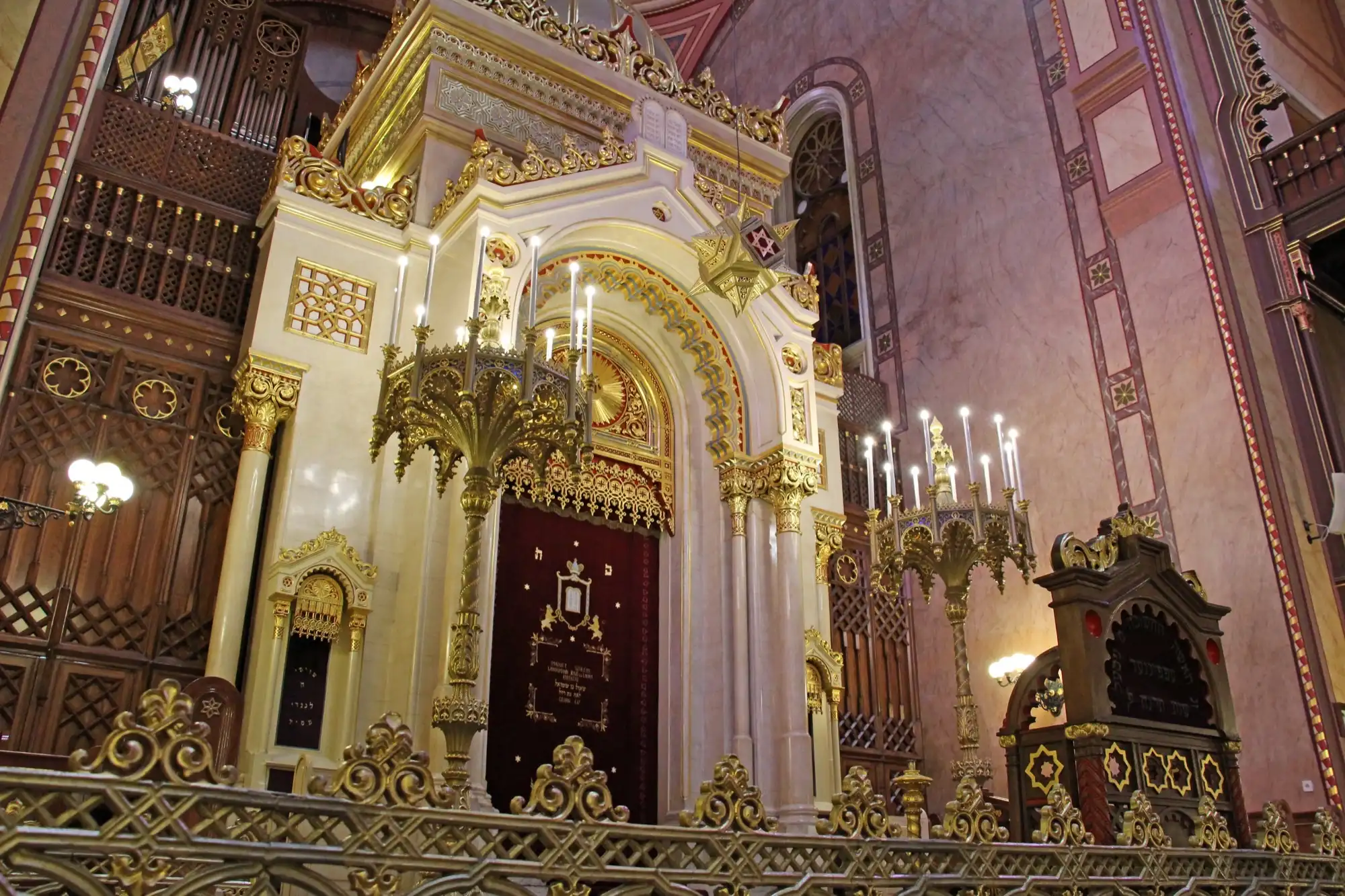 The white and gold Ark of the Dohány Street Synagogue, designed by Frigyes Feszl, with its dark curtain, candelabra and a carved pulpit to the right