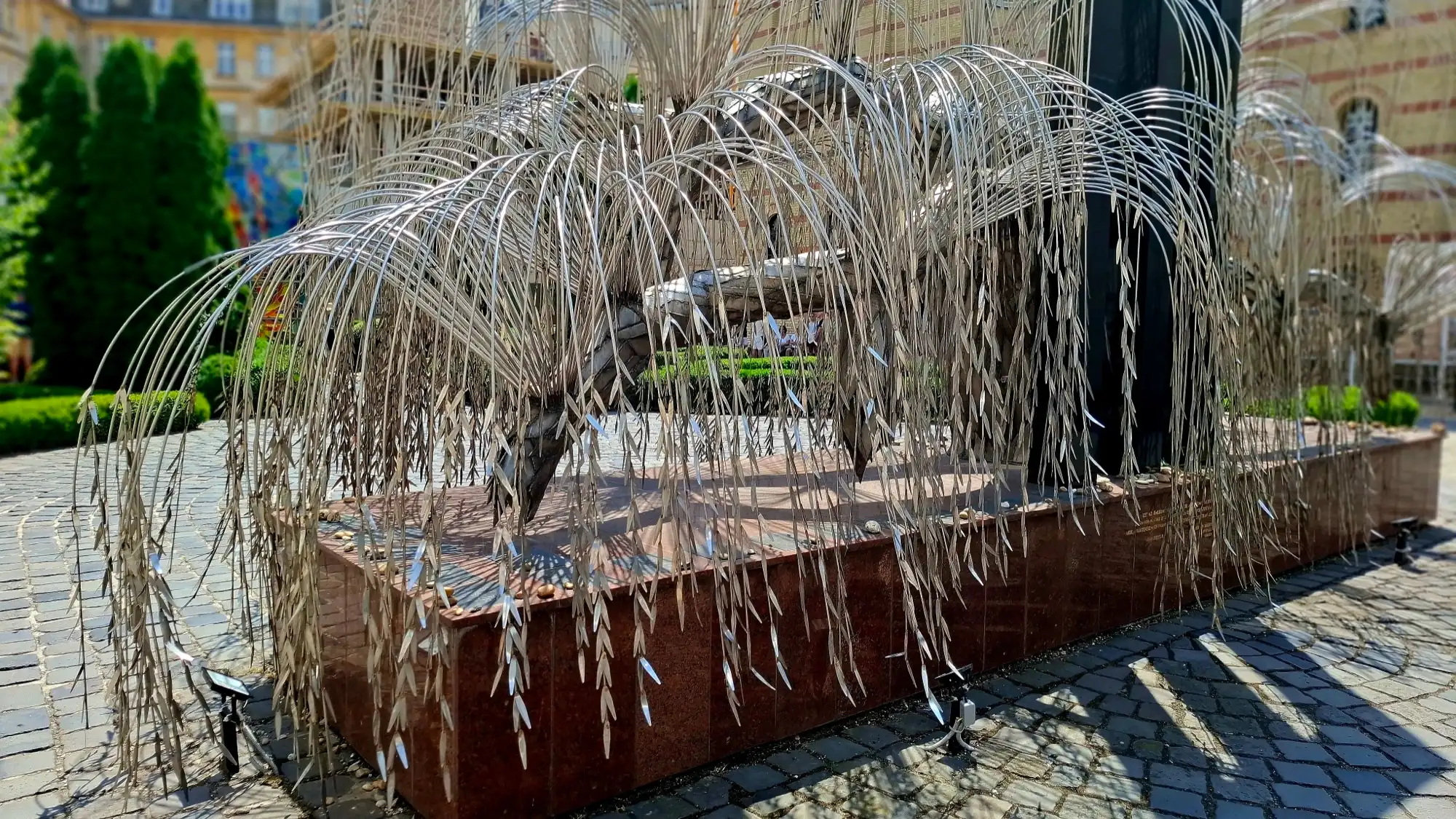 Close view of the metal leaves of the Tree of Life memorial hanging over its red granite base in the Raoul Wallenberg Memorial Park