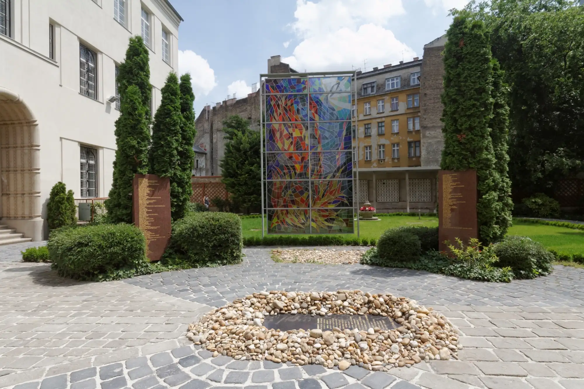 The Raoul Wallenberg Memorial Park behind the Dohány Street Synagogue, with a stained-glass memorial panel, tablets of rescuers' names and a bed of pebbles around a plaque