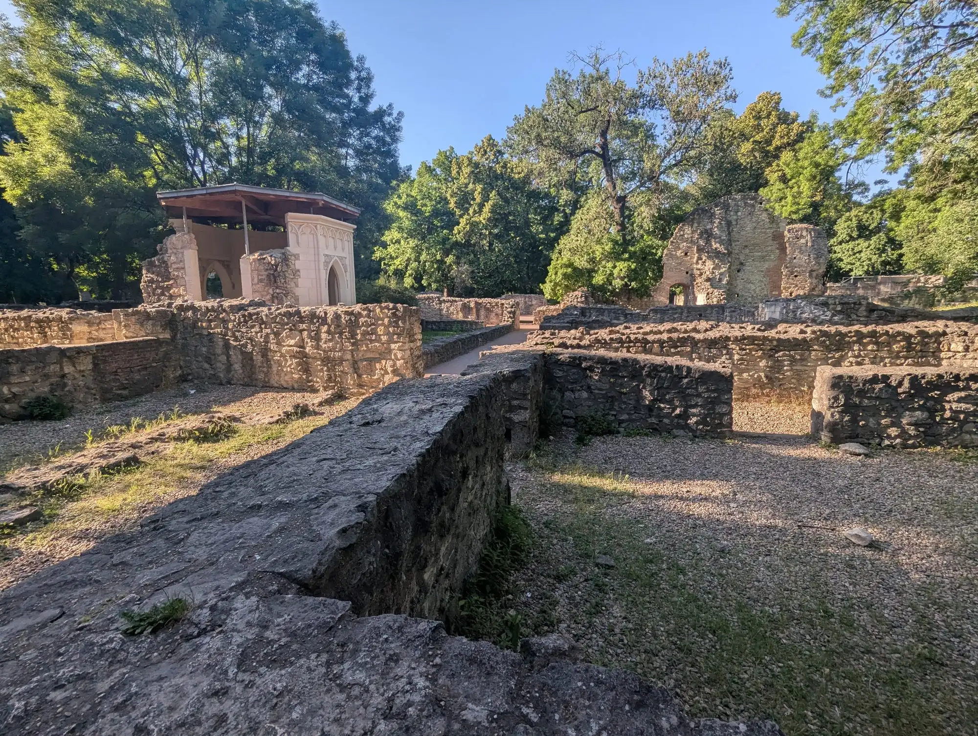 The ruins of the Dominican convent on Margaret Island, low stone walls and gravel paths between them, with the canopy over Saint Margaret's grave slab behind