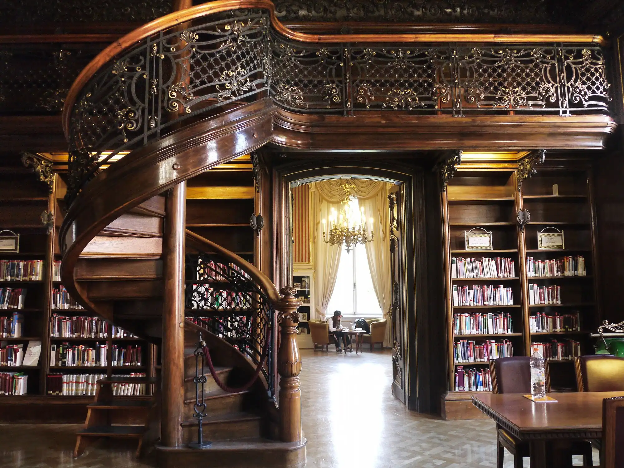 A reading room in the Ervin Szabó Library in Budapest, with dark panelled walls, book-lined shelves and a carved wooden spiral staircase up to a balustraded gallery