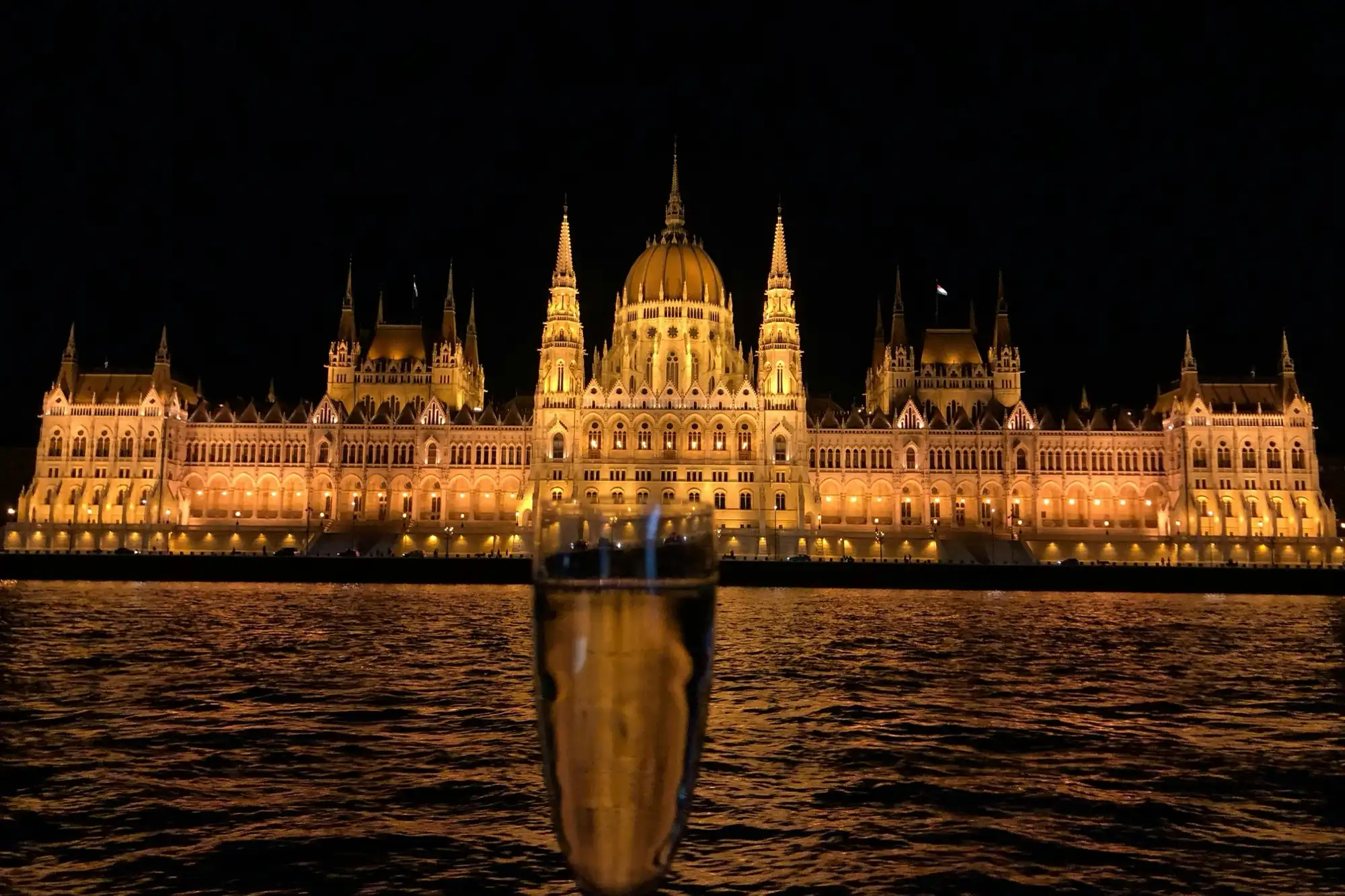 A glass raised on deck with the floodlit Parliament across the river on the evening cruise