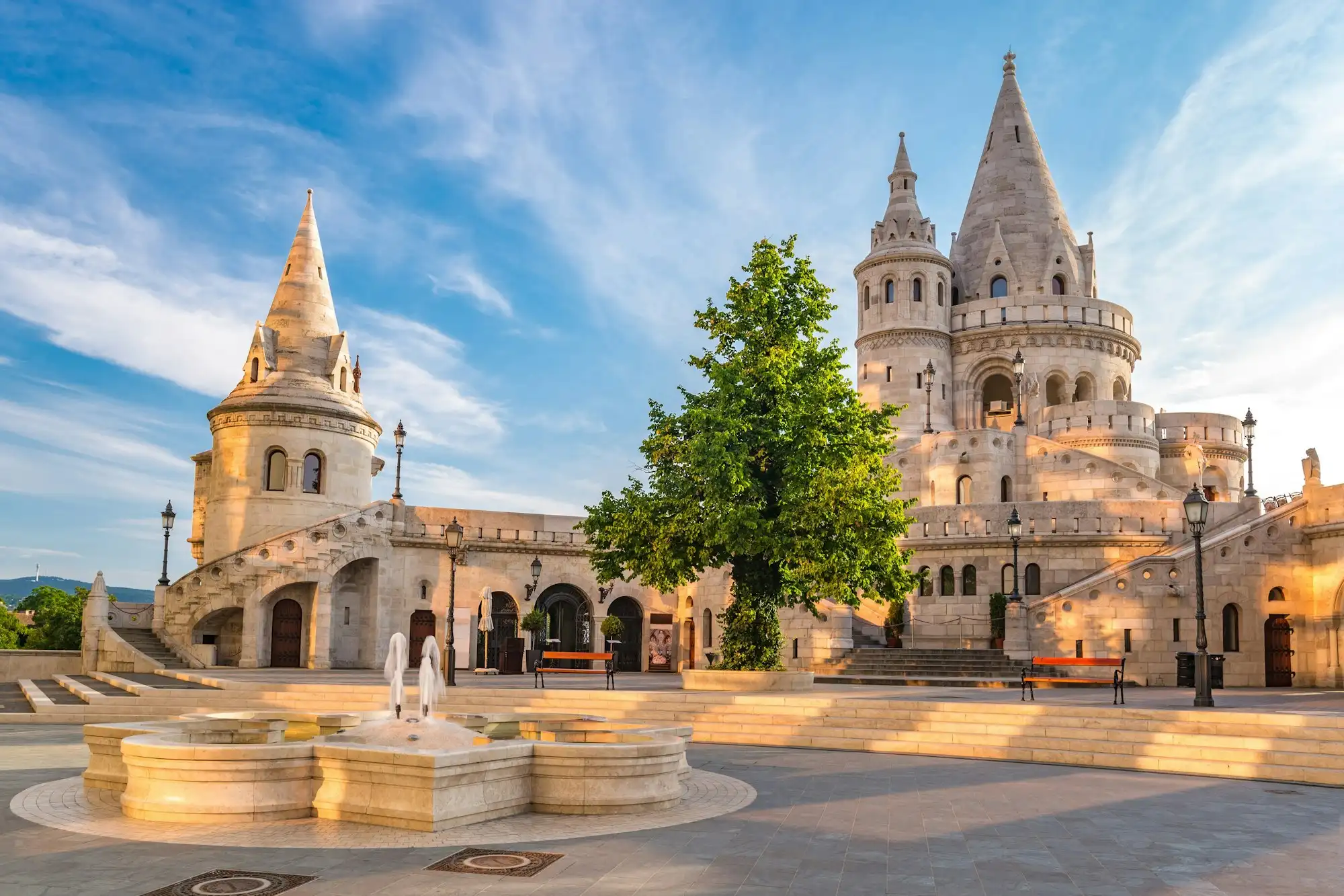 The tall north tower group of Fisherman's Bastion seen from the square, with conical stone roofs and open stairways in evening light