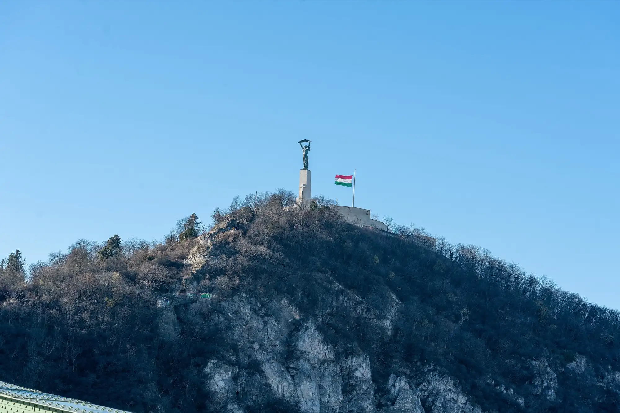 Gellért Hill in Budapest seen from below, with the Liberty Statue and the Hungarian flag on the summit