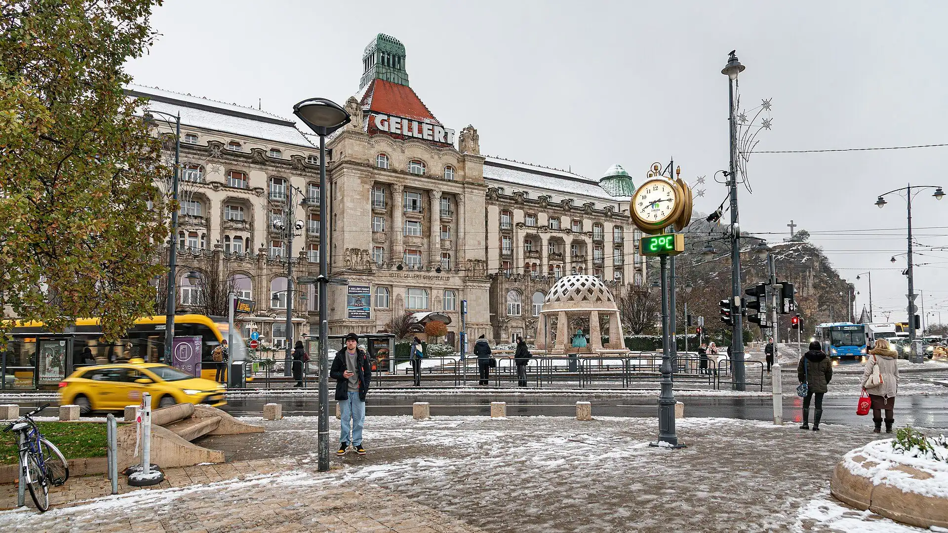 Szent Gellért tér in winter, with the Gellért Hotel's domed front, the square's clock and taxis in the foreground