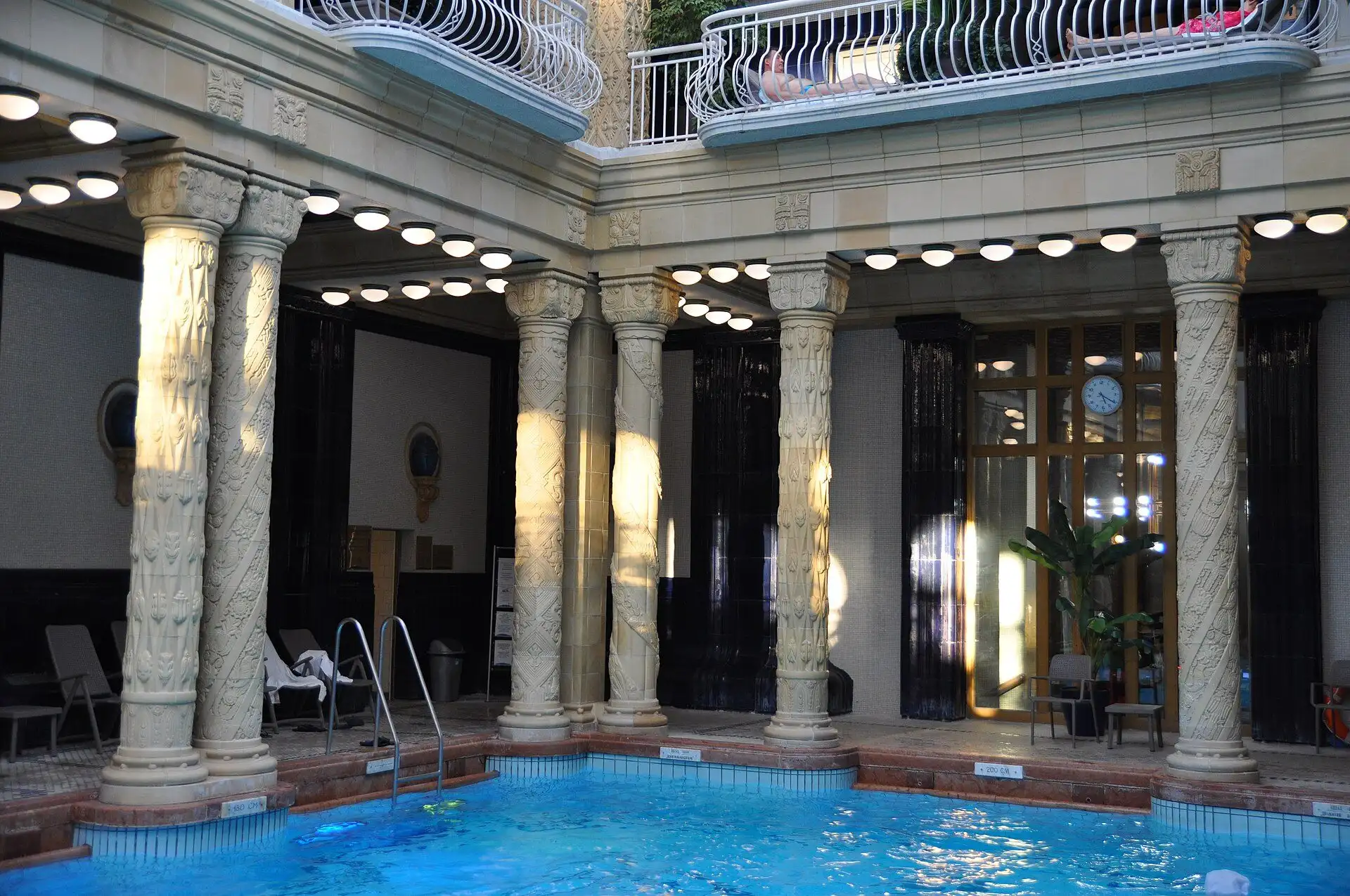 The indoor swimming pool at Gellért Thermal Bath, lined with carved columns and a gallery, with a swimmer in the water