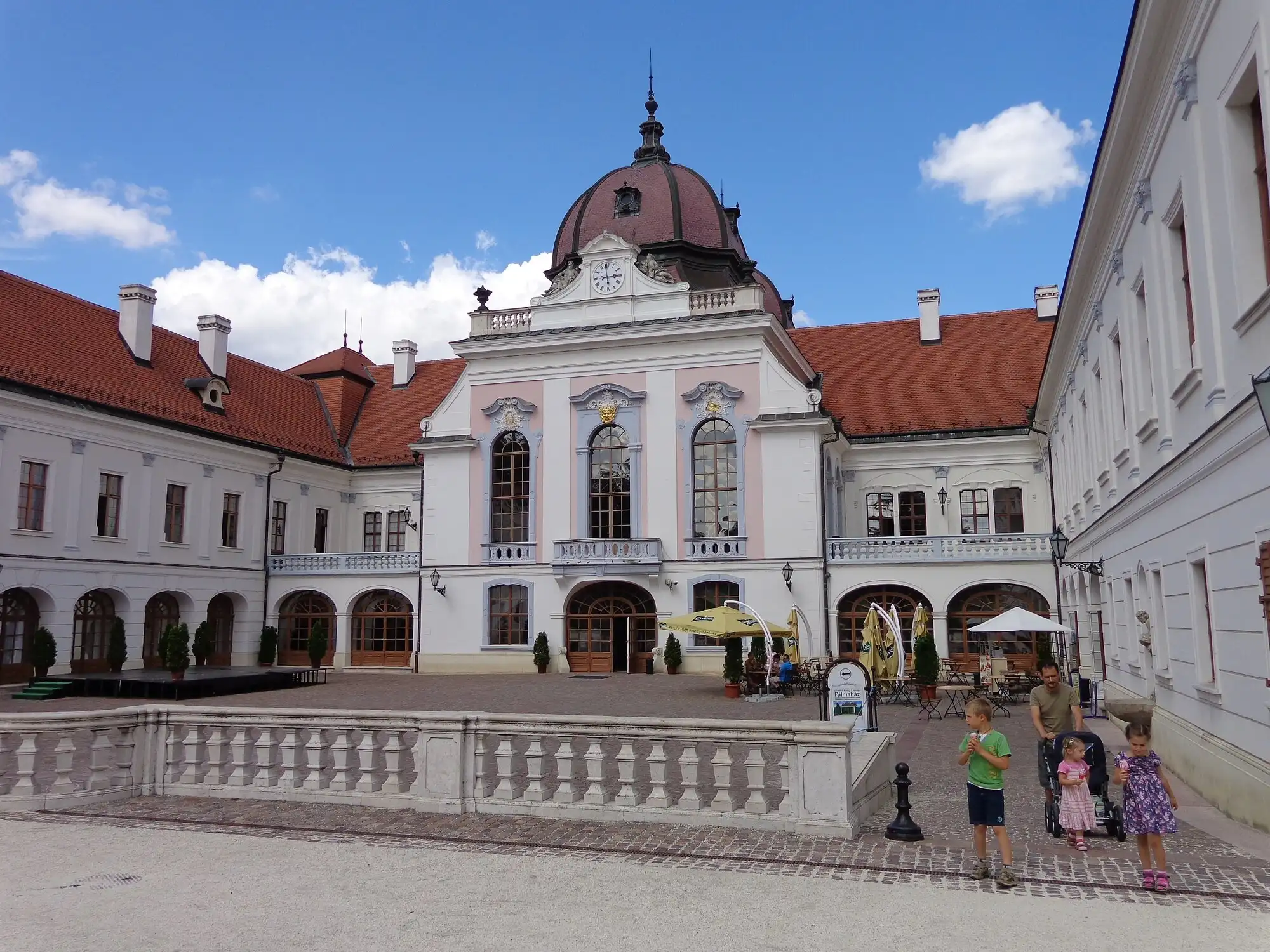 The pink and white baroque main building of the Royal Palace of Gödöllő, its domed centre block above an arcaded courtyard