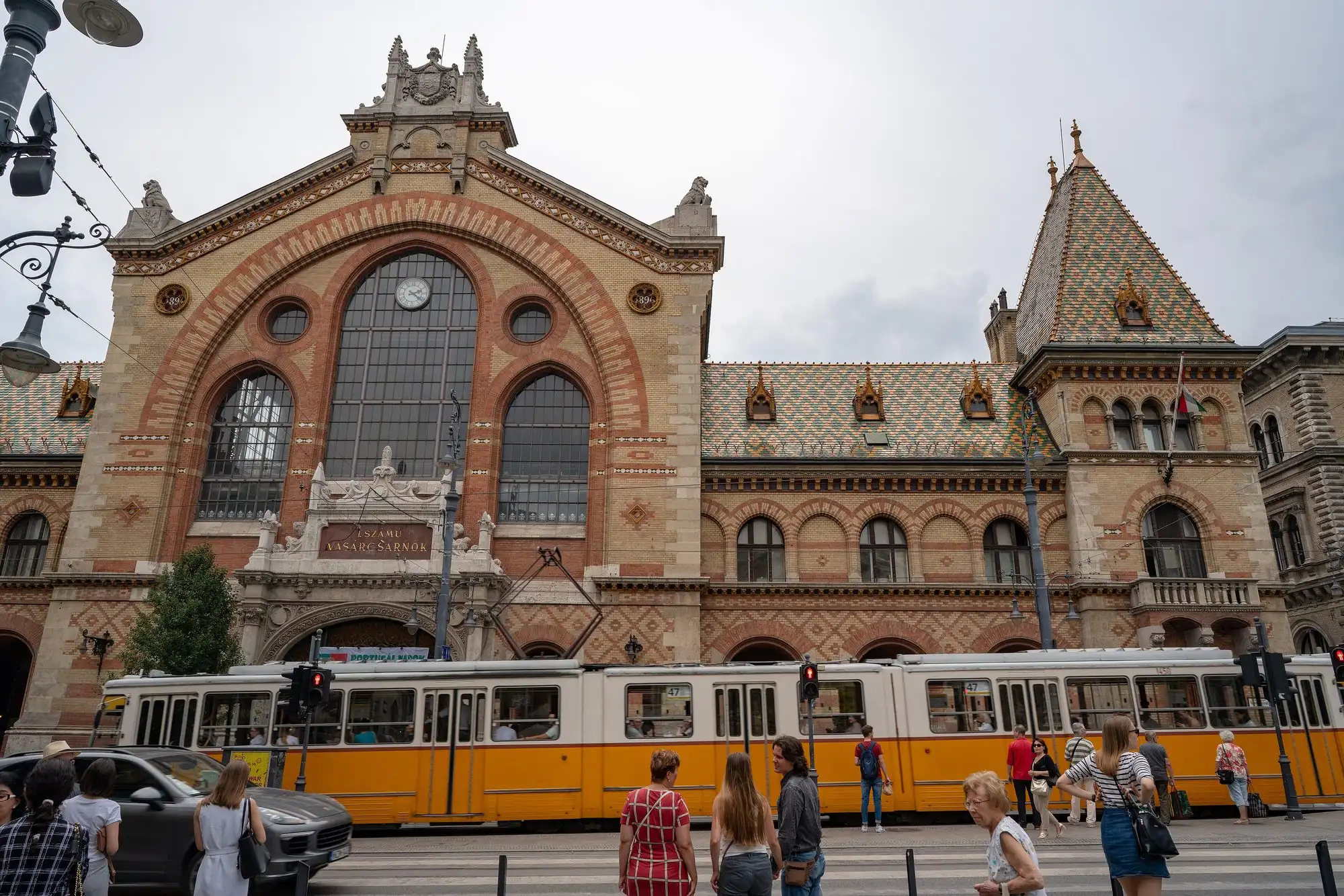 The main front of the Great Market Hall on Fővám tér in Budapest, with a yellow tram passing the entrance
