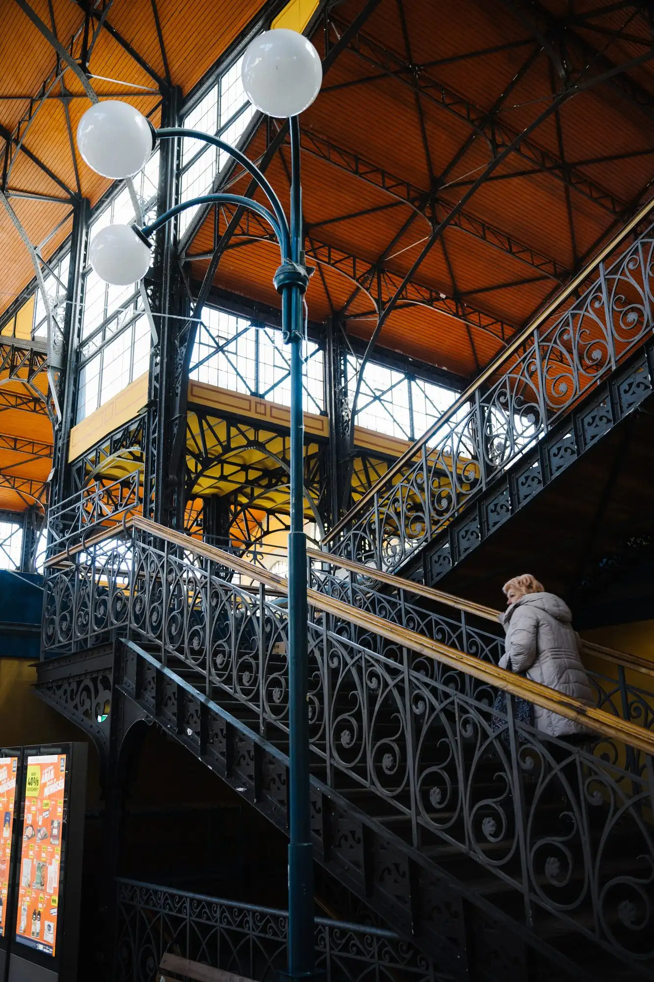 One of the ornamental cast-iron staircases inside the Great Market Hall in Budapest, with a woman climbing to the gallery
