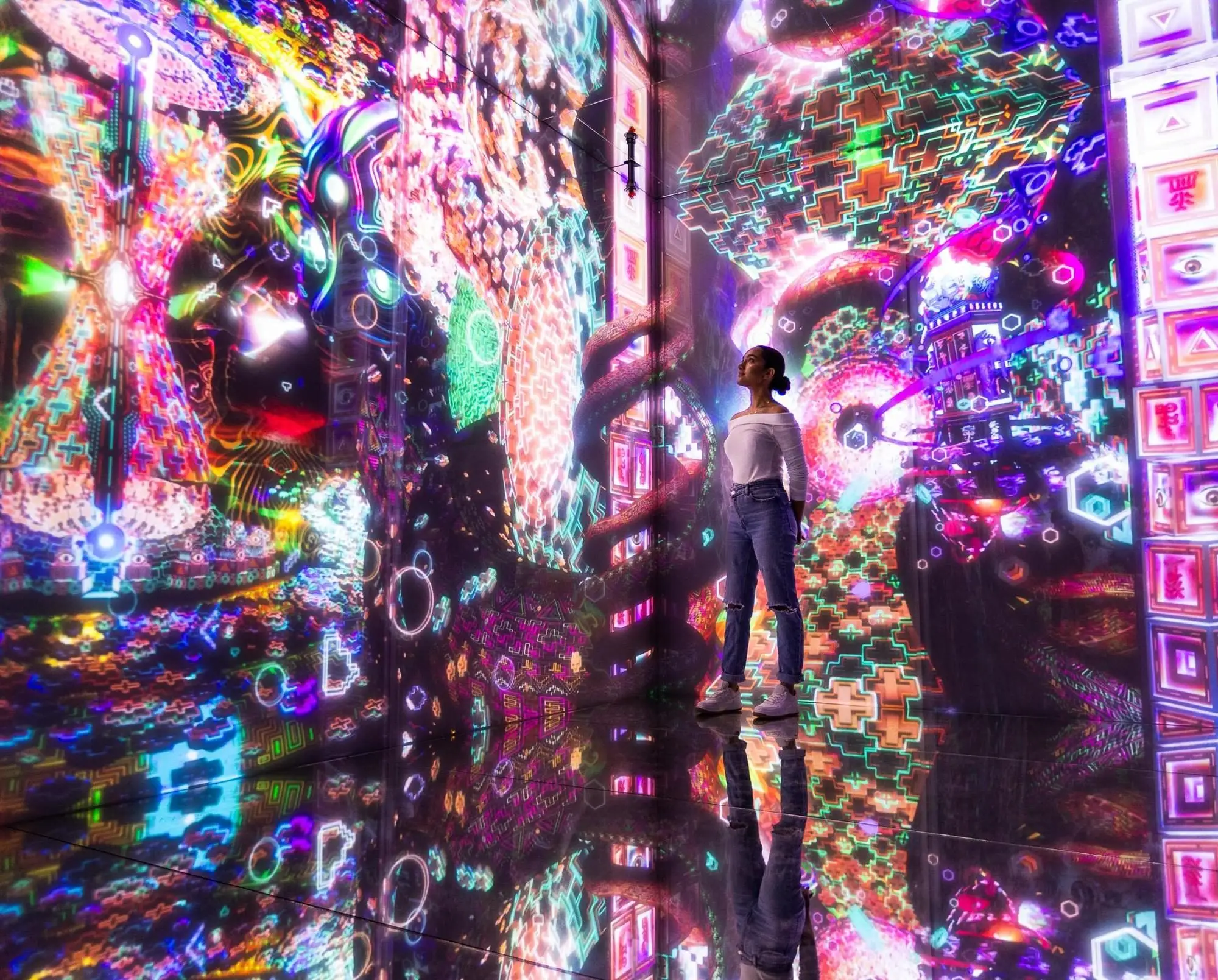 A visitor standing in a mirrored room at Cinema Mystica in Budapest, surrounded by brightly coloured projected patterns on the walls and floor