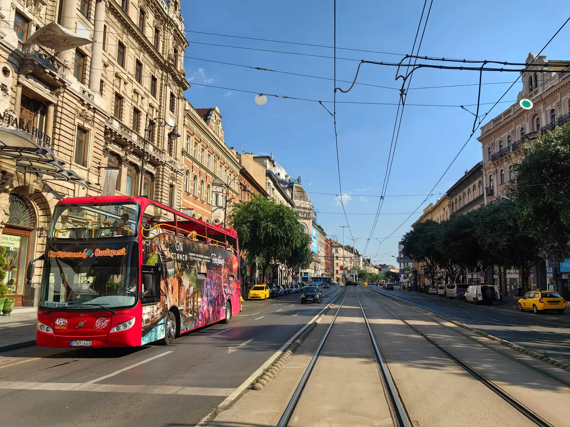 A red City Sightseeing open-top double-decker bus on a Pest boulevard in Budapest