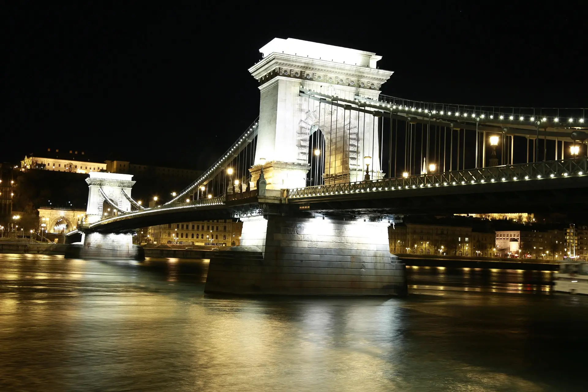 The Széchenyi Chain Bridge lit up at night over the Danube, with Buda Castle on the hill behind