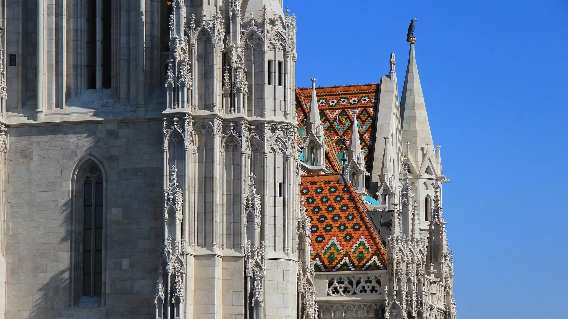 The white stone tower of Matthias Church beside its diamond-patterned Zsolnay tile roof, against a blue sky