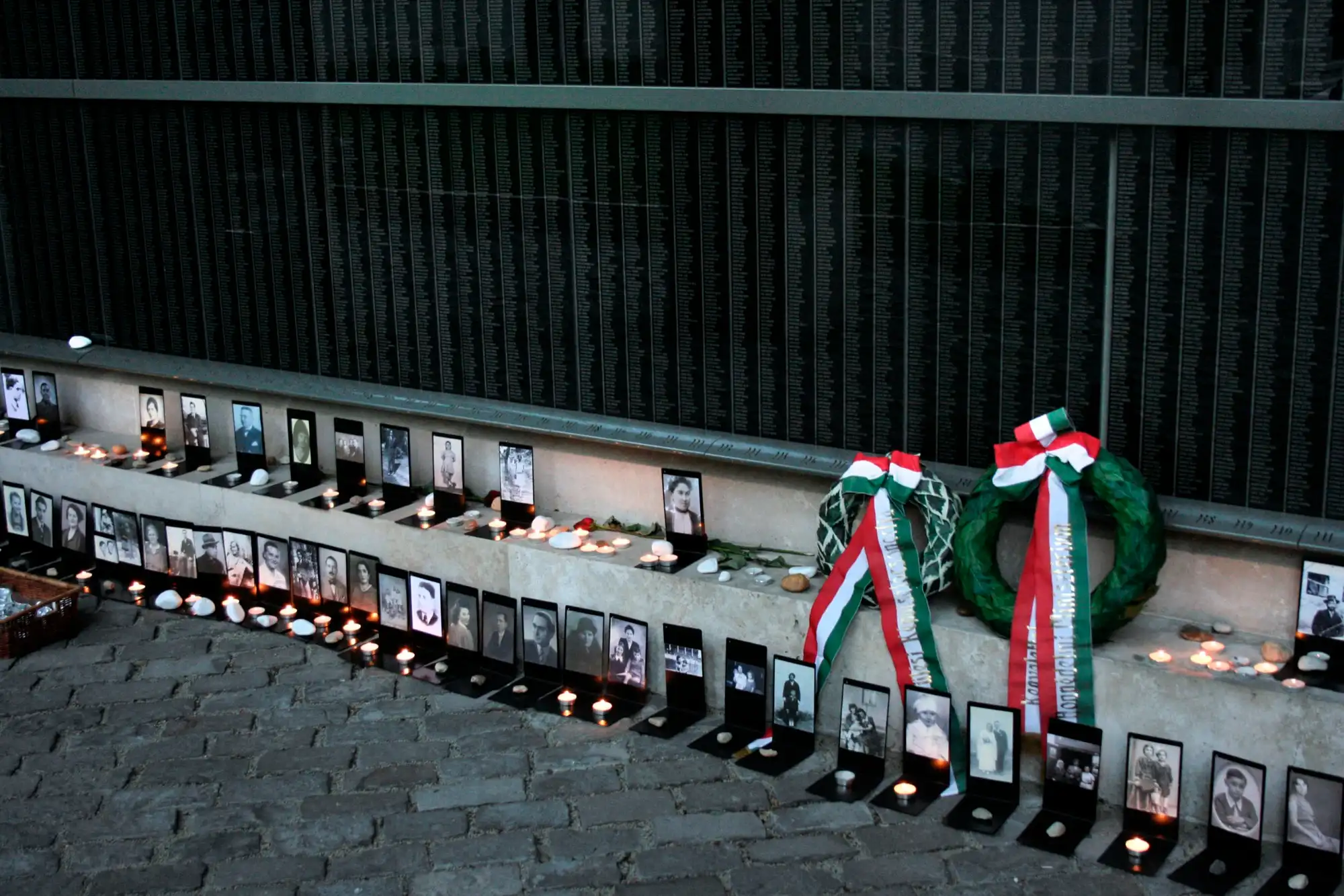 The Memorial Wall of Victims in the courtyard of the Holocaust Memorial Center on Páva utca, with family photographs, candles and wreaths placed along its base