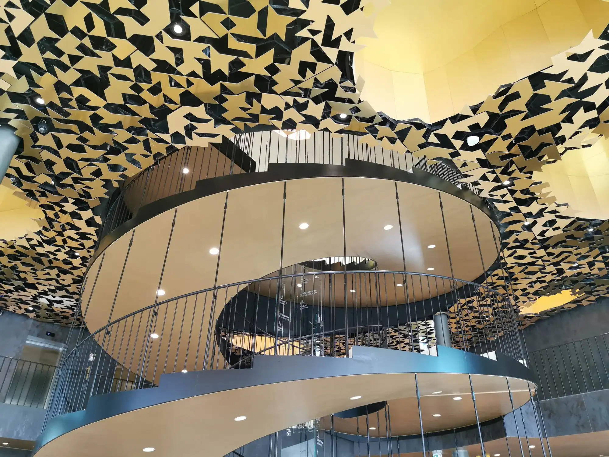 Inside the House of Hungarian Music in Budapest, looking up at the golden leaf-patterned ceiling and the curved opening around the spiral staircase