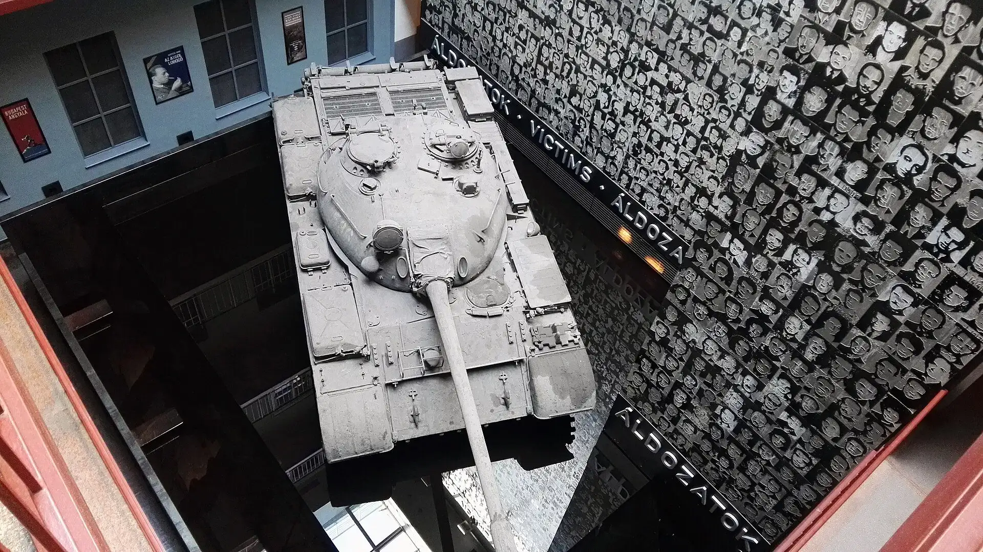 The Soviet T-54 tank in the glassed-over atrium of the House of Terror Museum, seen from a gallery above, with the wall of victims' portraits behind it