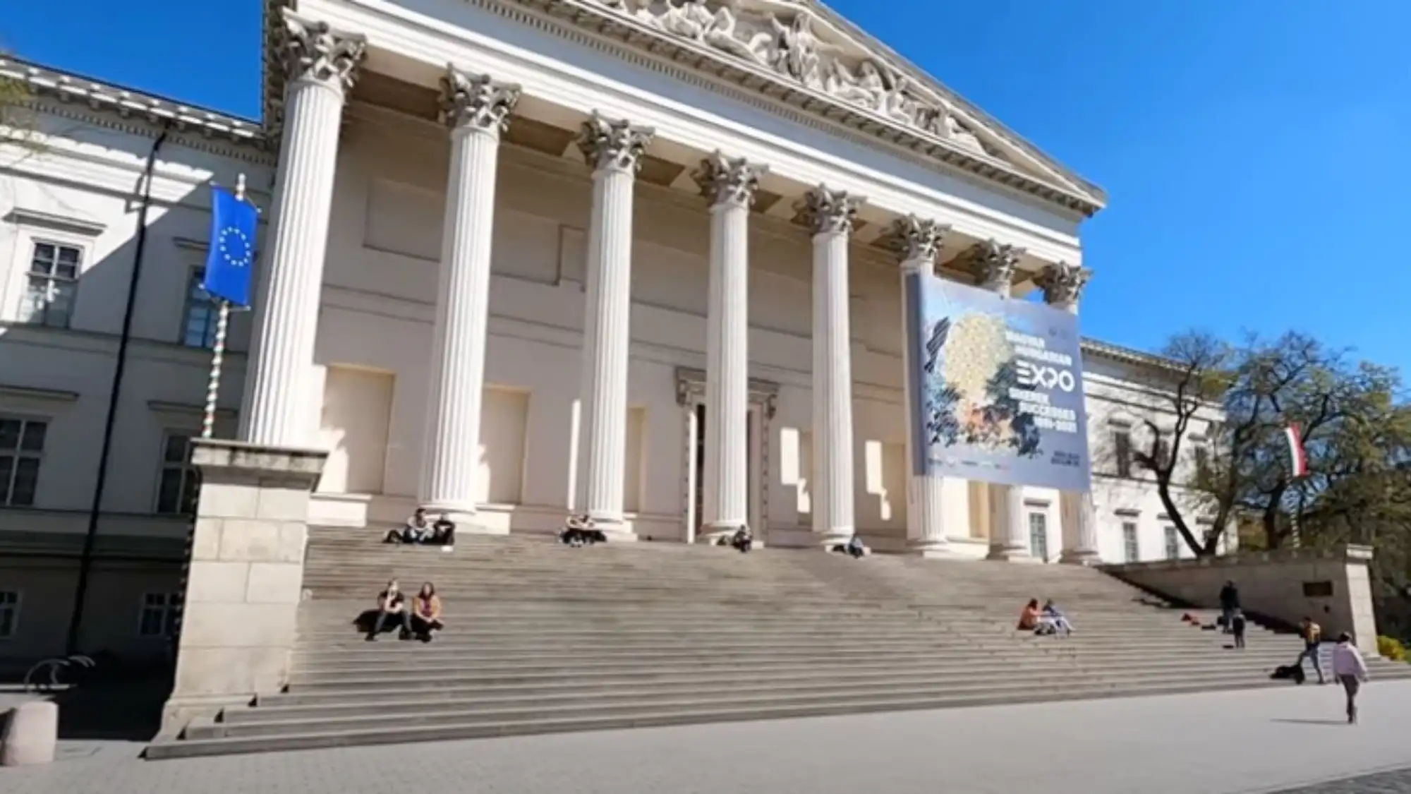 The columned main entrance of the Hungarian National Museum in Budapest, with visitors sitting on the steps