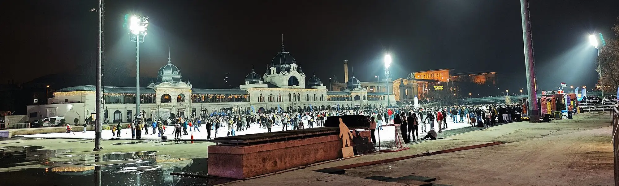 Crowds of skaters under floodlights on the City Park Ice Rink in Budapest at night, in front of the lit domed rink building