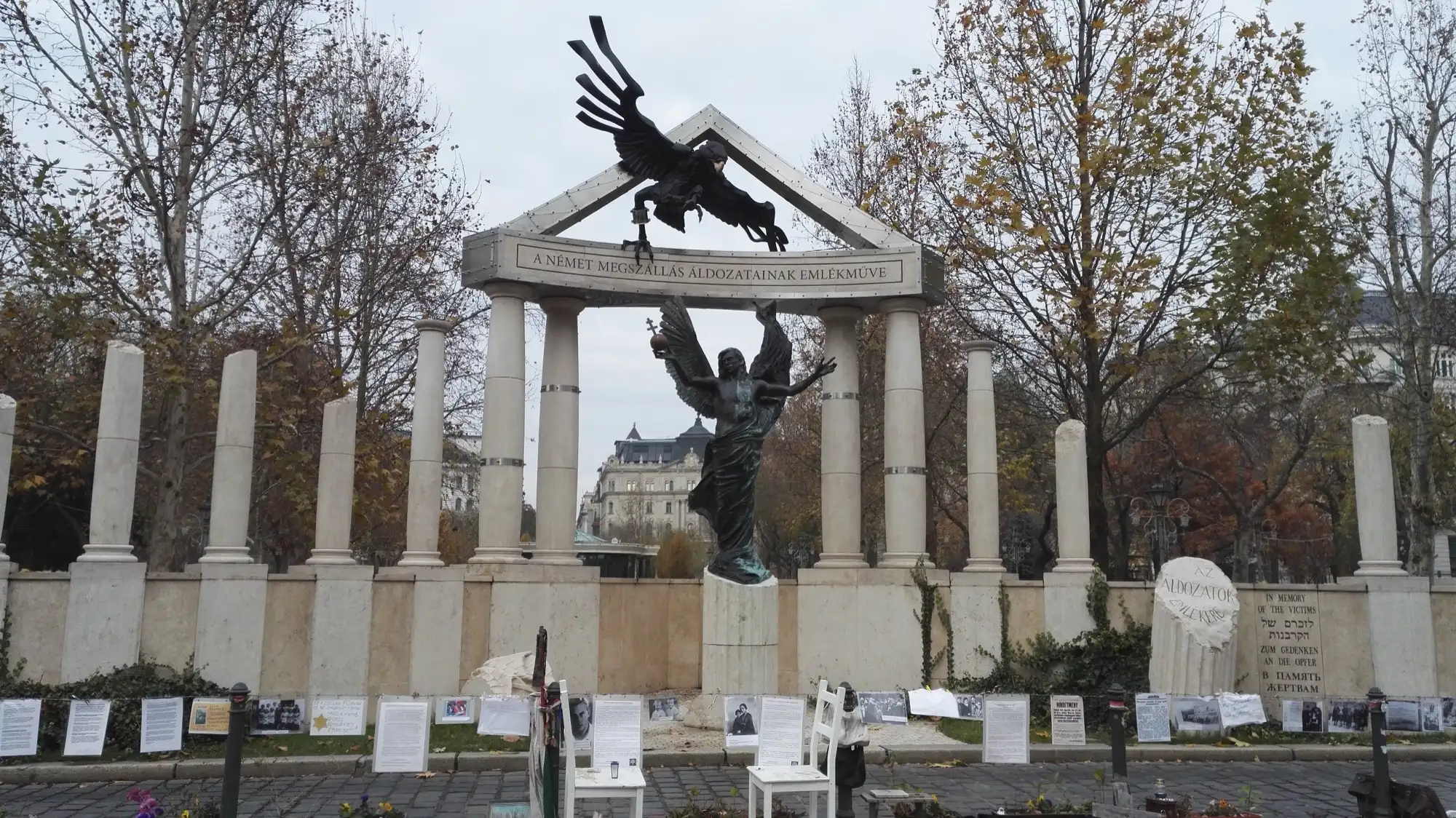 The memorial to the victims of the German occupation on Liberty Square in Budapest, an angel beneath a swooping eagle, with the citizens' Living Memorial of photographs and personal objects laid out in front