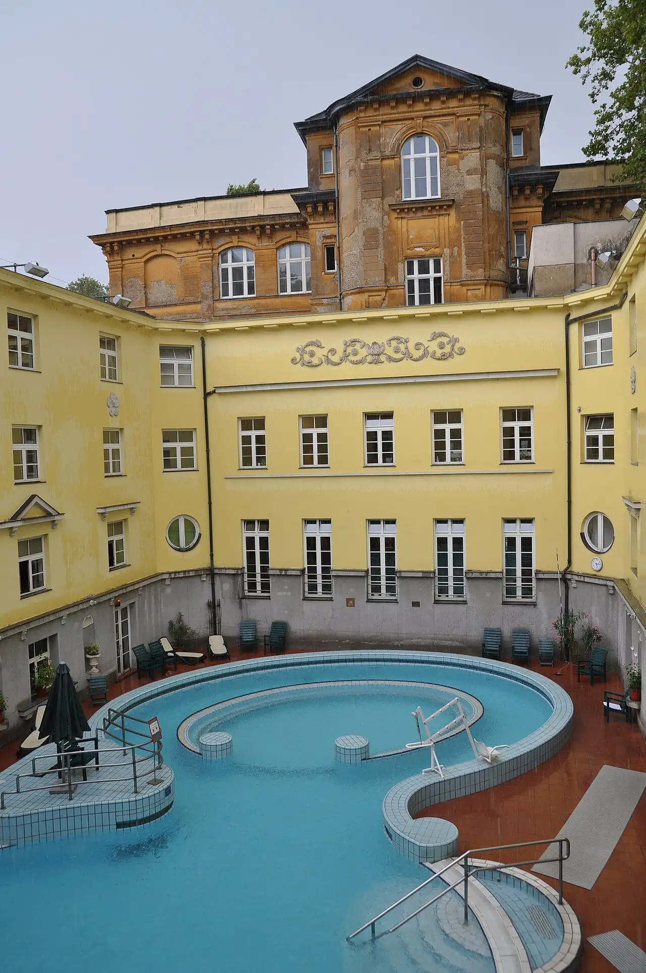 The outdoor adventure pool in a courtyard at Lukács Thermal Bath, with the yellow bath wings and an older brick building behind