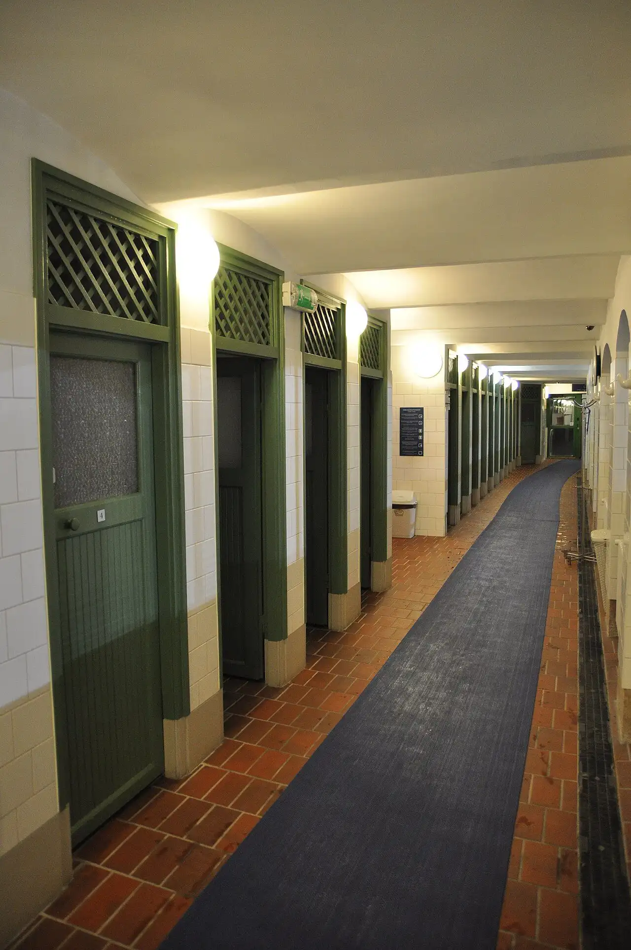 A corridor of numbered green changing-cabin doors with white tiled walls at Lukács Thermal Bath