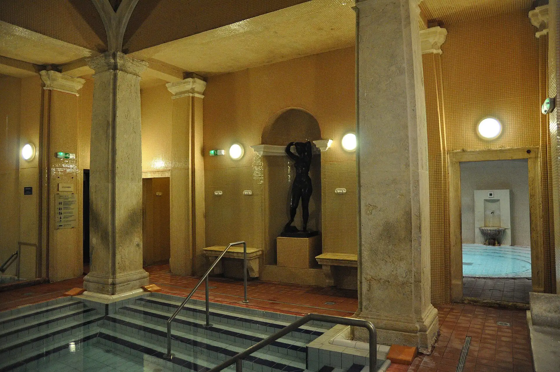 Indoor thermal section at Lukács Thermal Bath, with stone pillars, gold tiling and steps down into a green-tiled pool