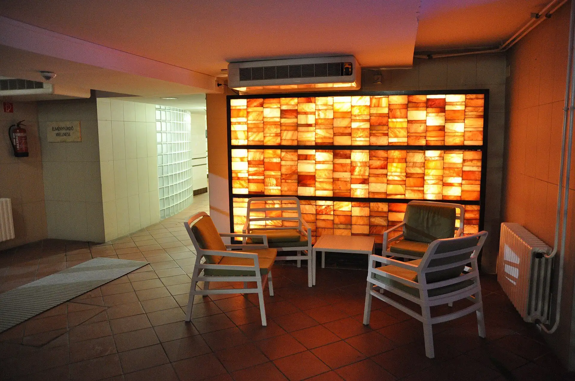 A backlit salt wall with four chairs and a low table in front of it at Lukács Thermal Bath