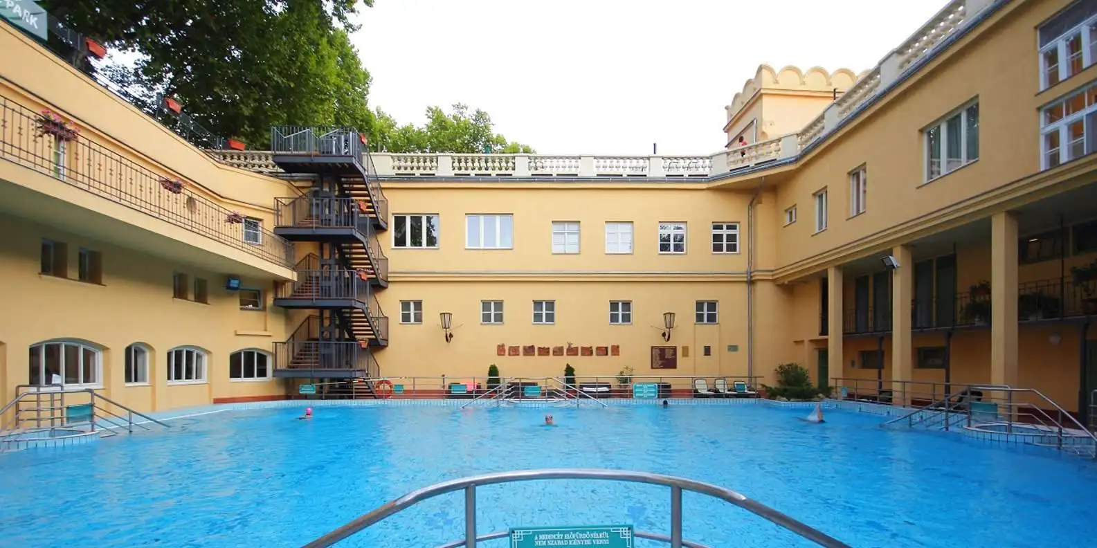 Outdoor swimming pool in a courtyard at Lukács Thermal Bath, with yellow wings and an iron staircase behind