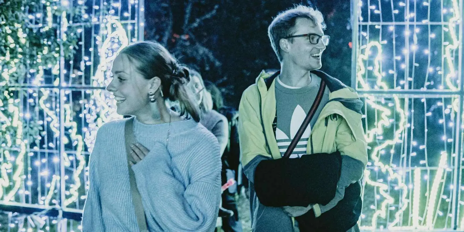 Visitors walking between walls of white and green light installations on the Lumina Park trail at night