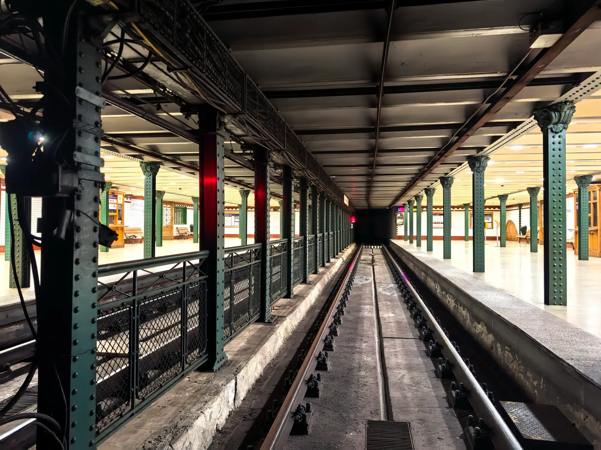 Looking down the track at Hősök tere station on the M1, riveted green columns and railings on both sides and the platforms beyond