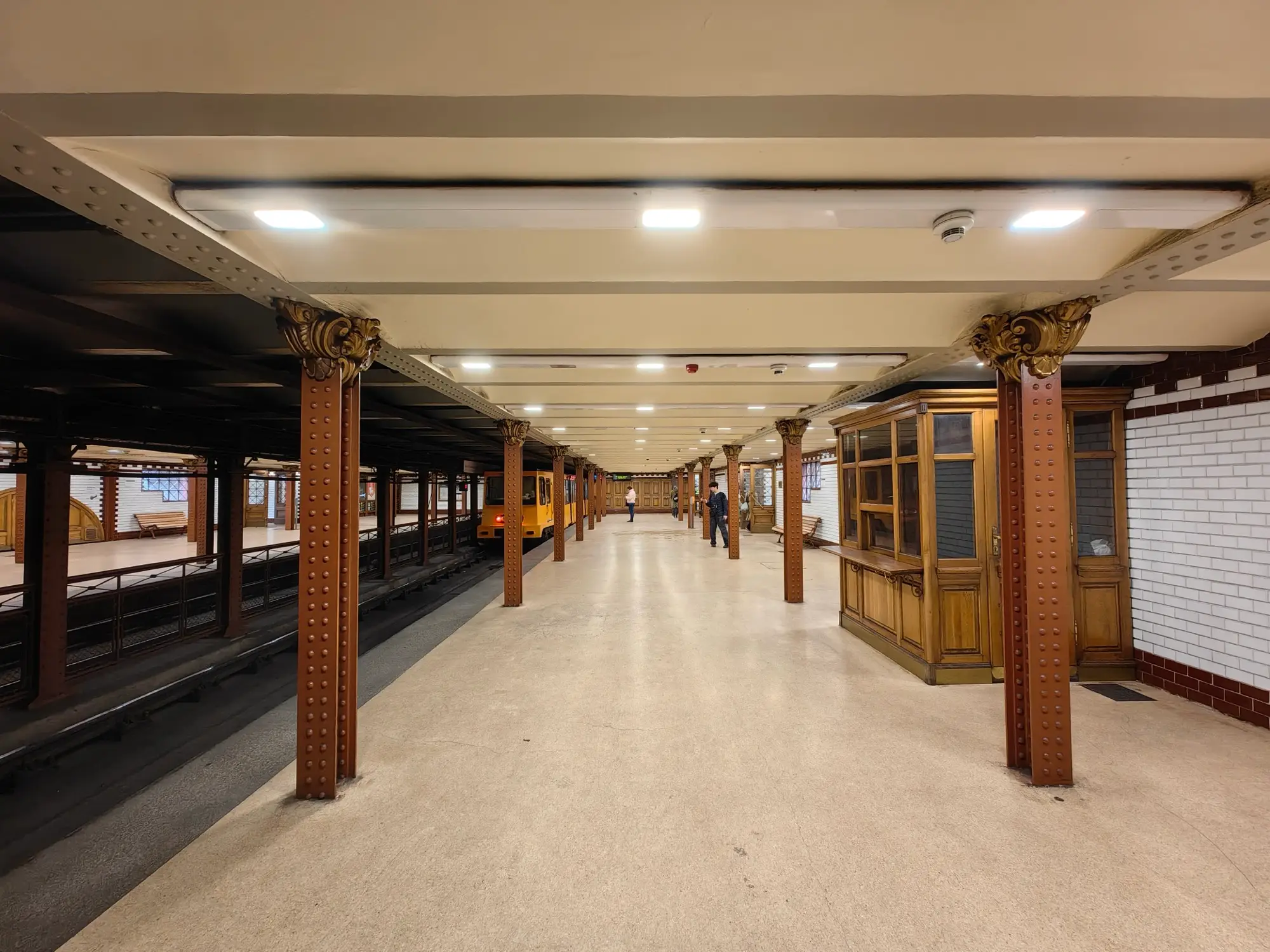 The platform of Opera station on Budapest's M1 Millennium Underground, with riveted iron columns, a timber ticket booth and white tiled walls