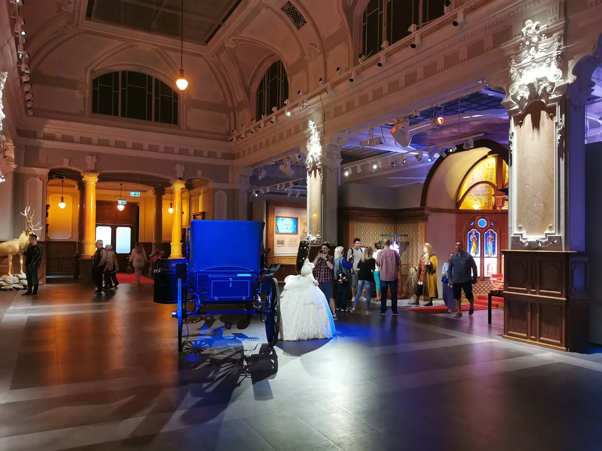The columned ticket hall of Madame Tussauds Budapest inside Palazzo Dorottya, with visitors at the desks under the palace ceiling
