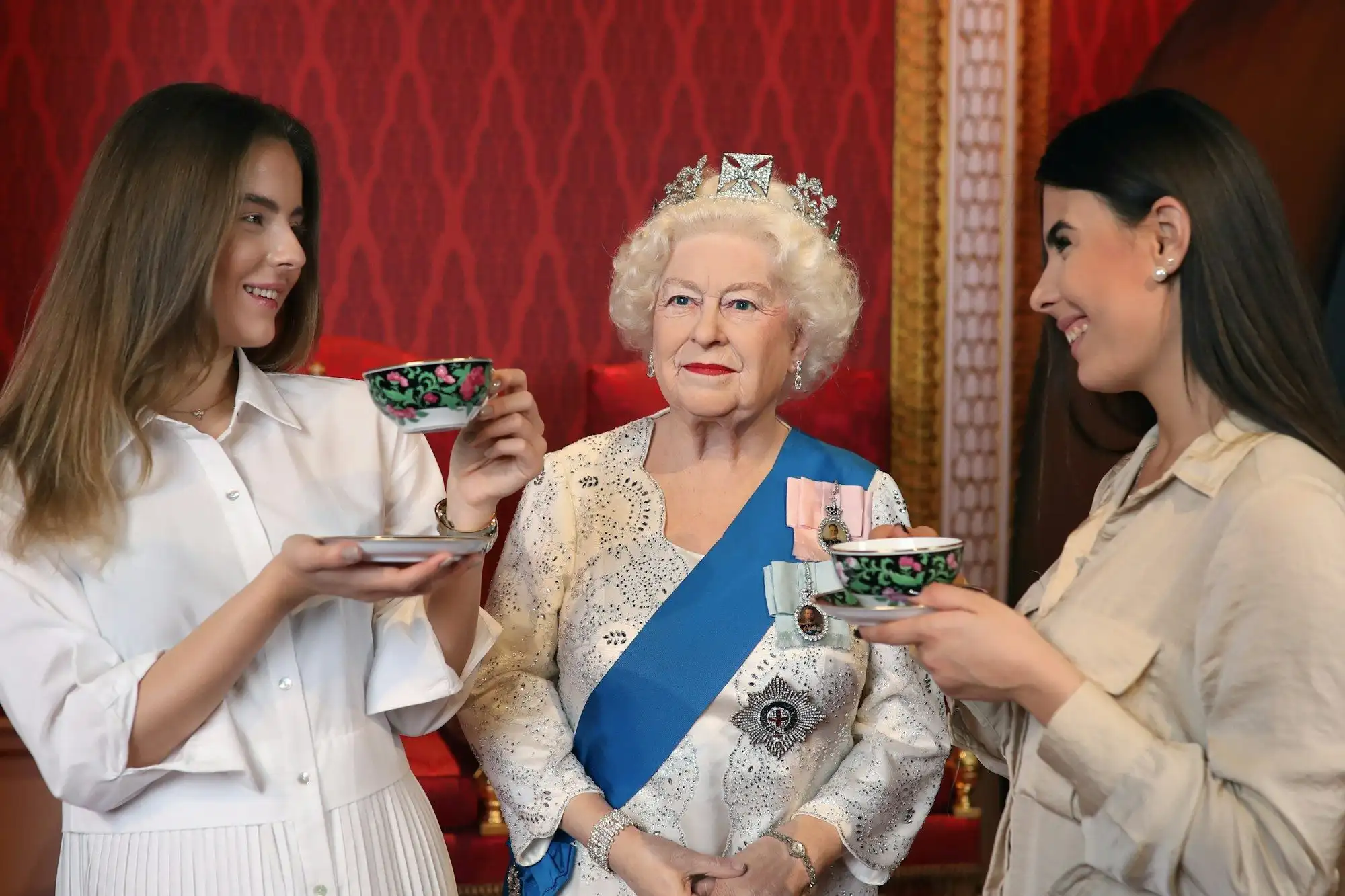 Two visitors taking tea beside the Queen Elizabeth II wax figure at Madame Tussauds Budapest