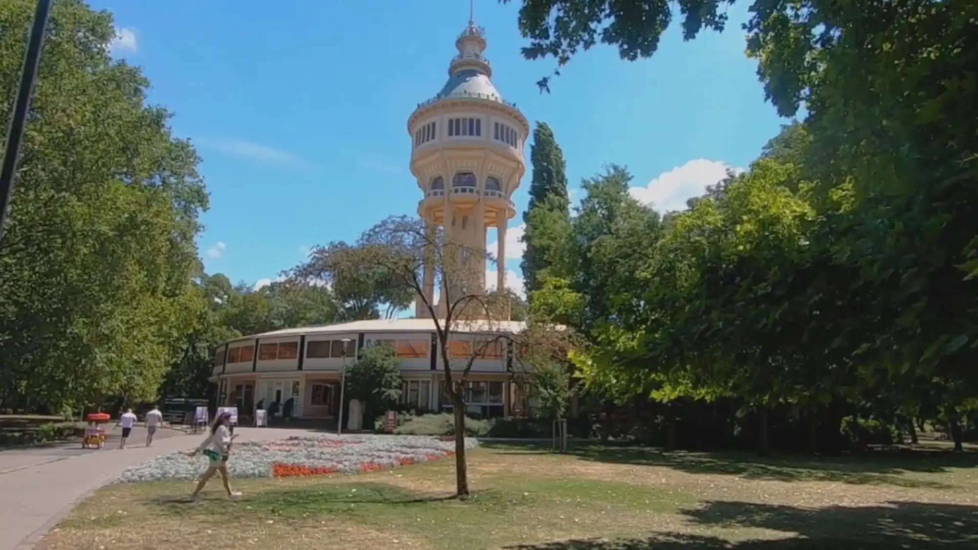 The Margaret Island Water Tower in Budapest, surrounded by trees and flower beds on a sunny day