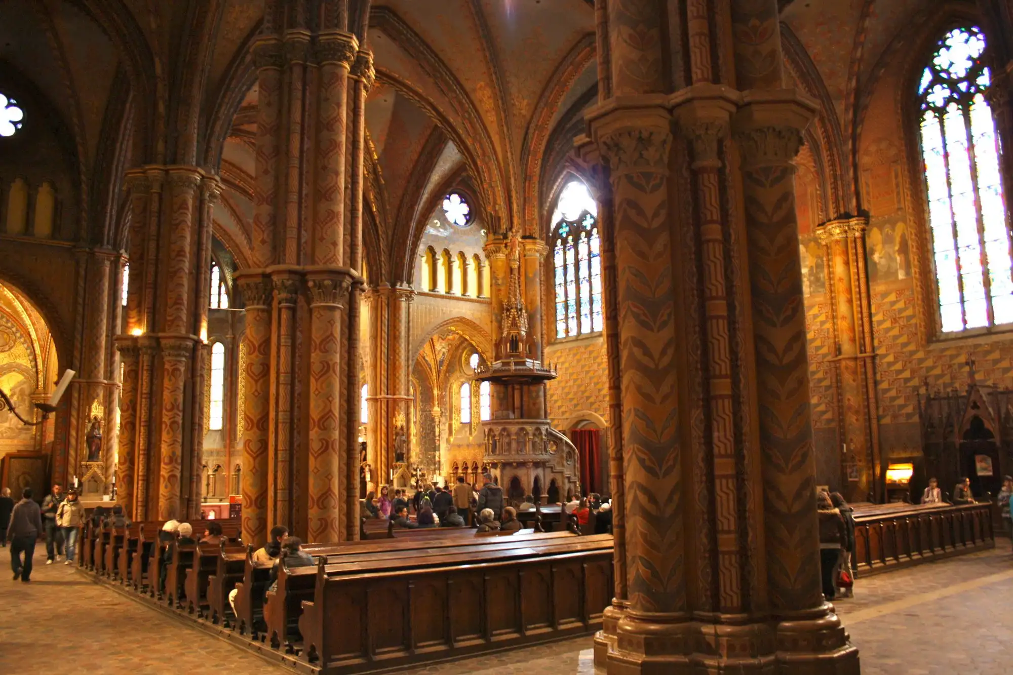 The nave of Matthias Church, with painted pillars, ornamented vaults and the pulpit, seen from the south aisle