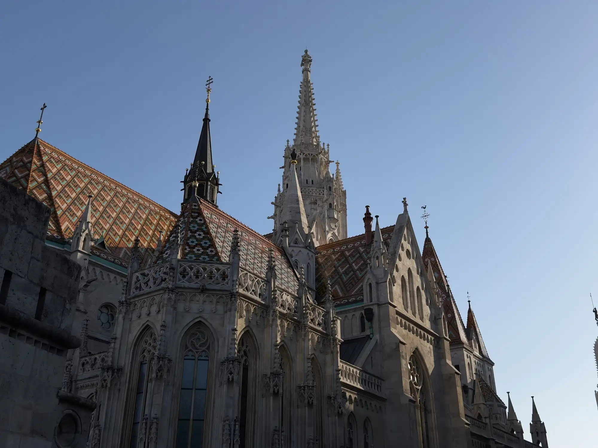 The diamond-patterned glazed Zsolnay tile roof of Matthias Church and its openwork Gothic Revival spire against a clear sky