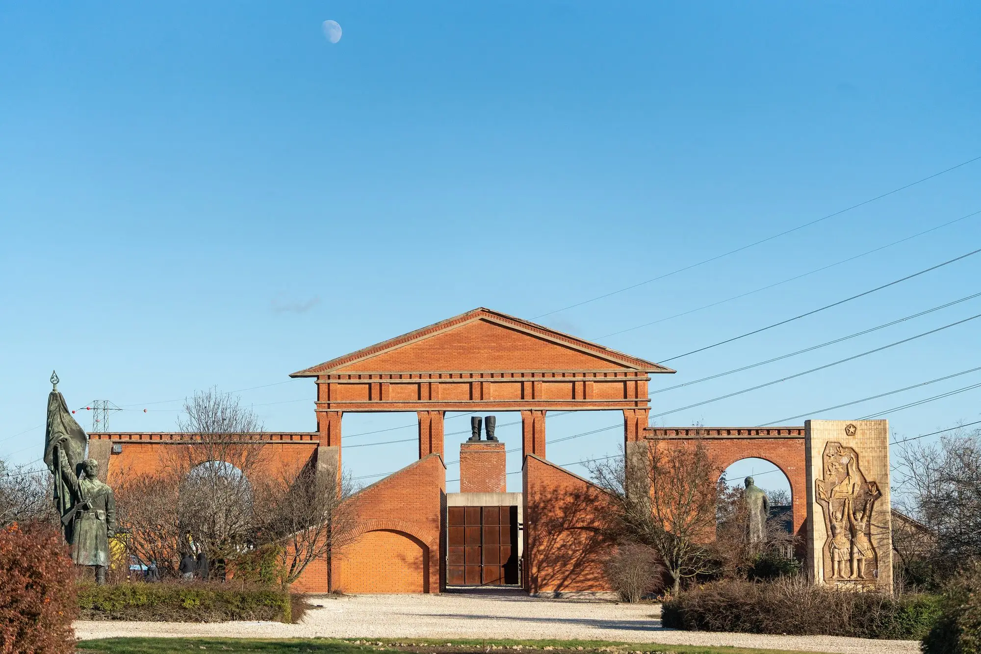 The red-brick entrance facade of Memento Park in Budapest, with a statue of Lenin in one arch and Marx and Engels in the other