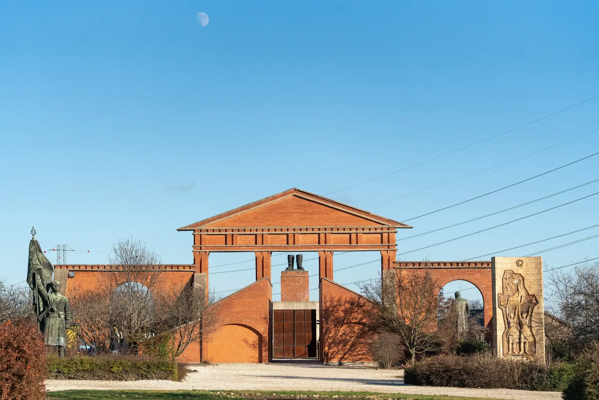 The red-brick entrance facade of Memento Park seen from the road, with statues in its arches